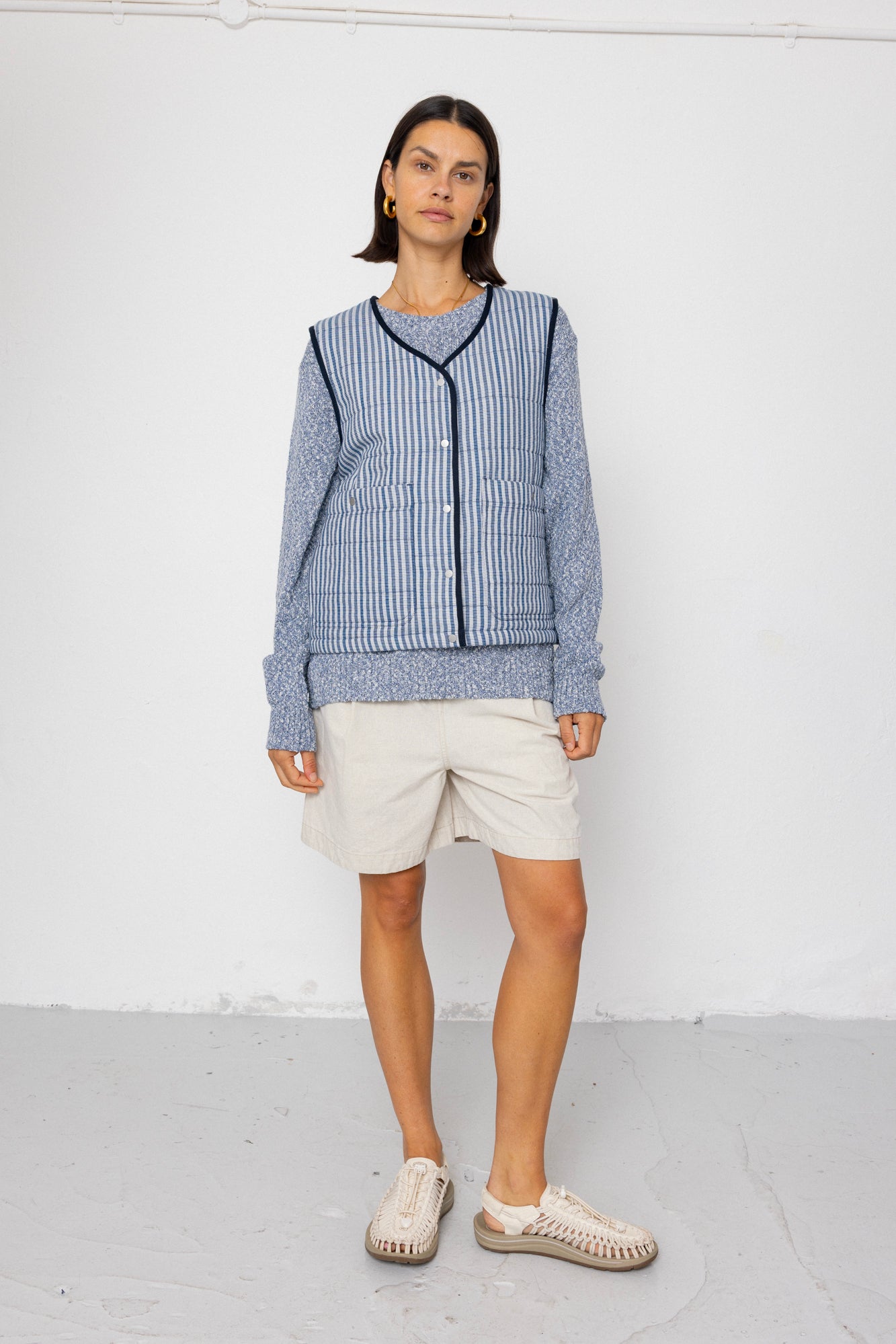 Woman wearing a blue striped vest and white shorts against a white background