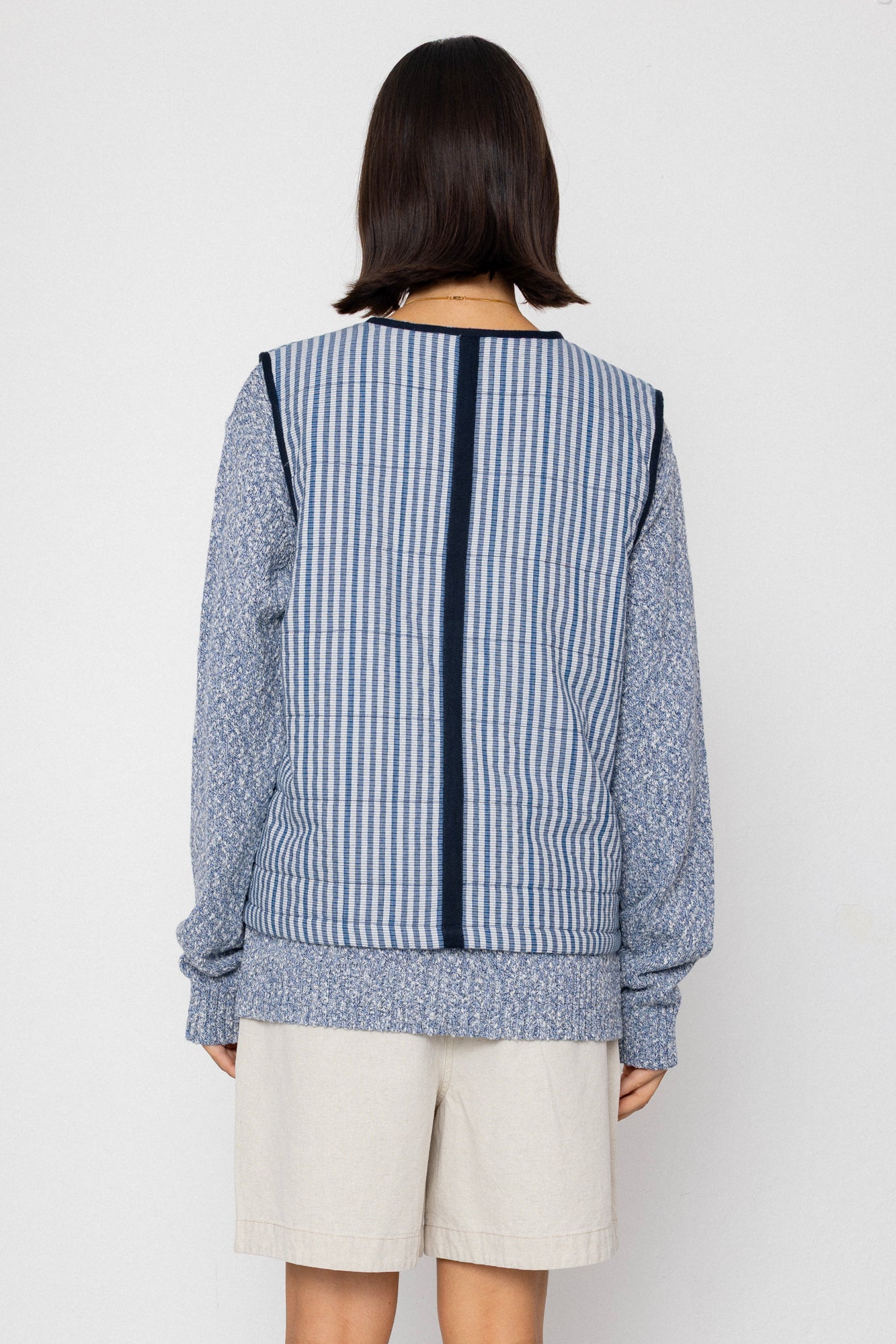 Person wearing a blue and white striped vest with a plain background
