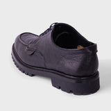 A single black leather lace-up shoe with a chunky lug sole, shown from a rear three-quarter angle on a light gray background.