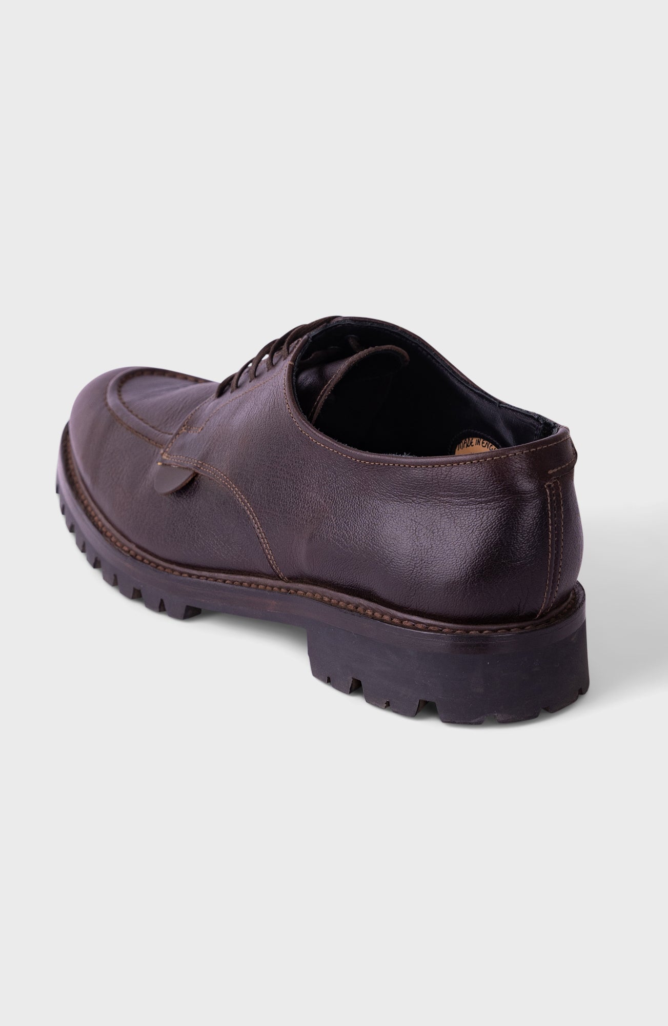 A dark brown leather lace-up shoe shown from a rear three-quarter angle against a light gray background.