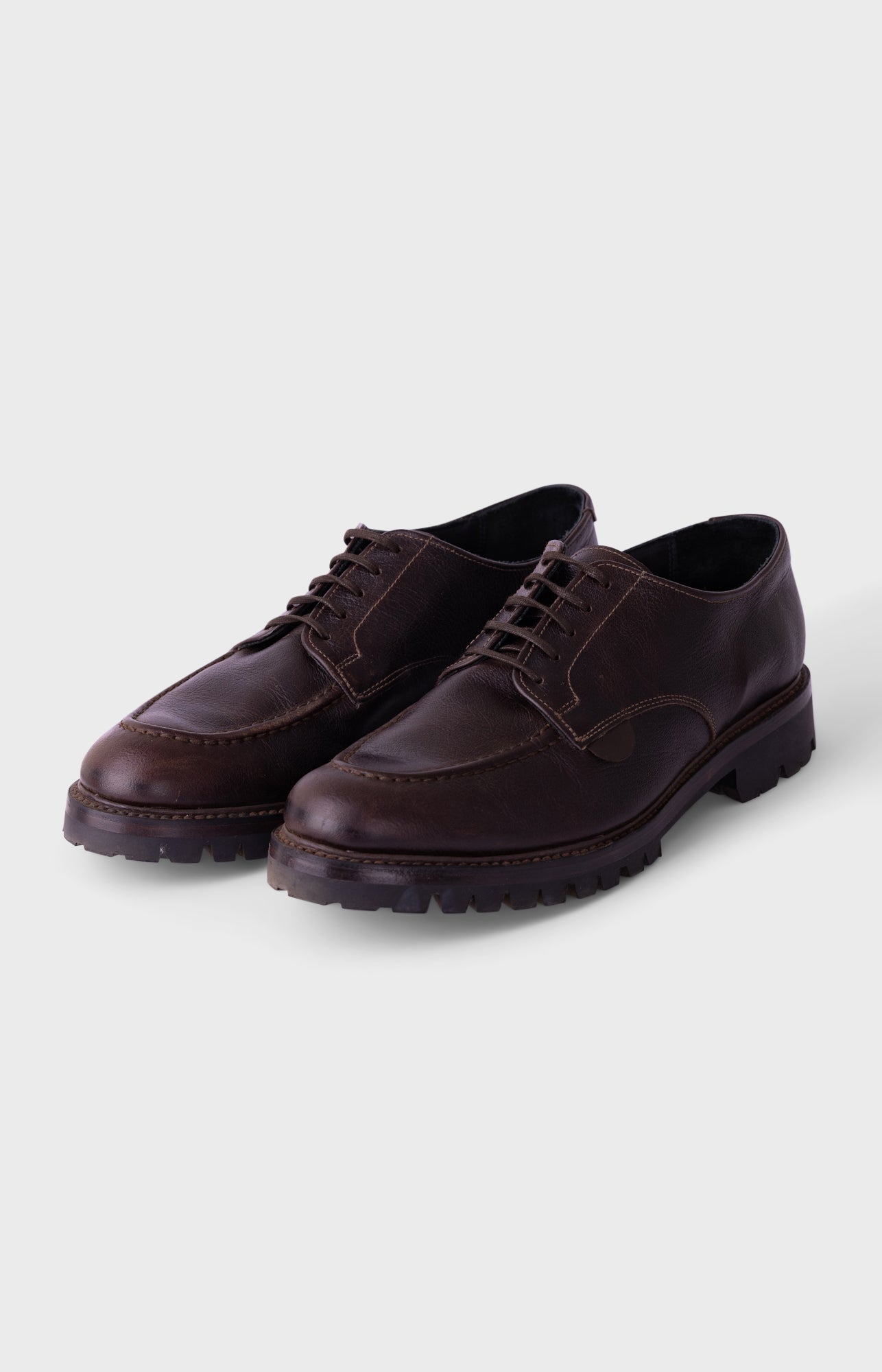 A pair of dark brown leather lace-up shoes with a rugged lug sole, displayed on a light gray background.