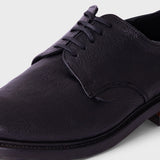 A close-up shot of a dark purple leather lace-up shoe on a light gray background.