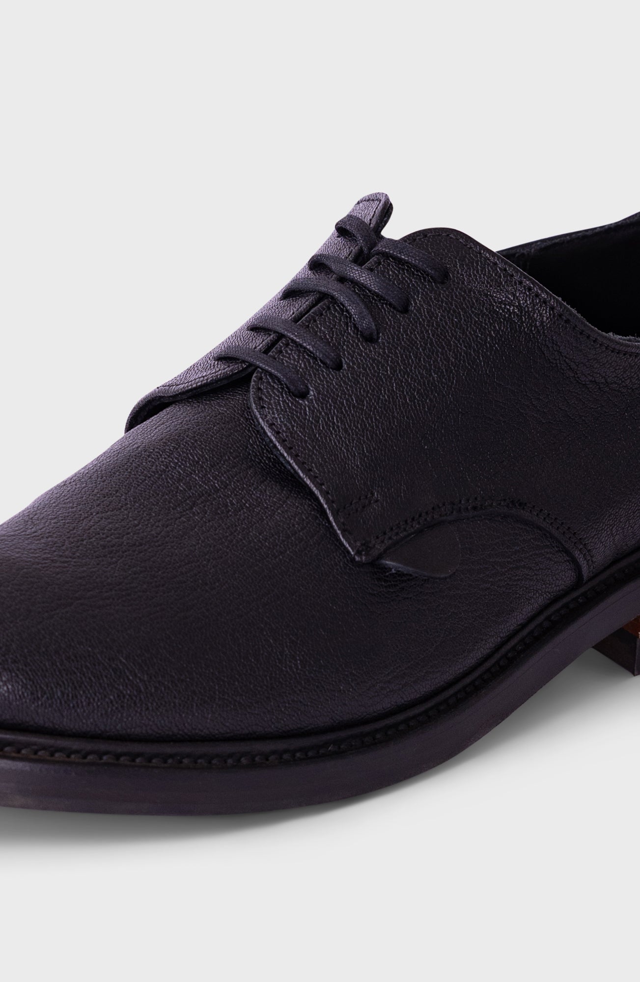 A close-up shot of a dark purple leather lace-up shoe on a light gray background.