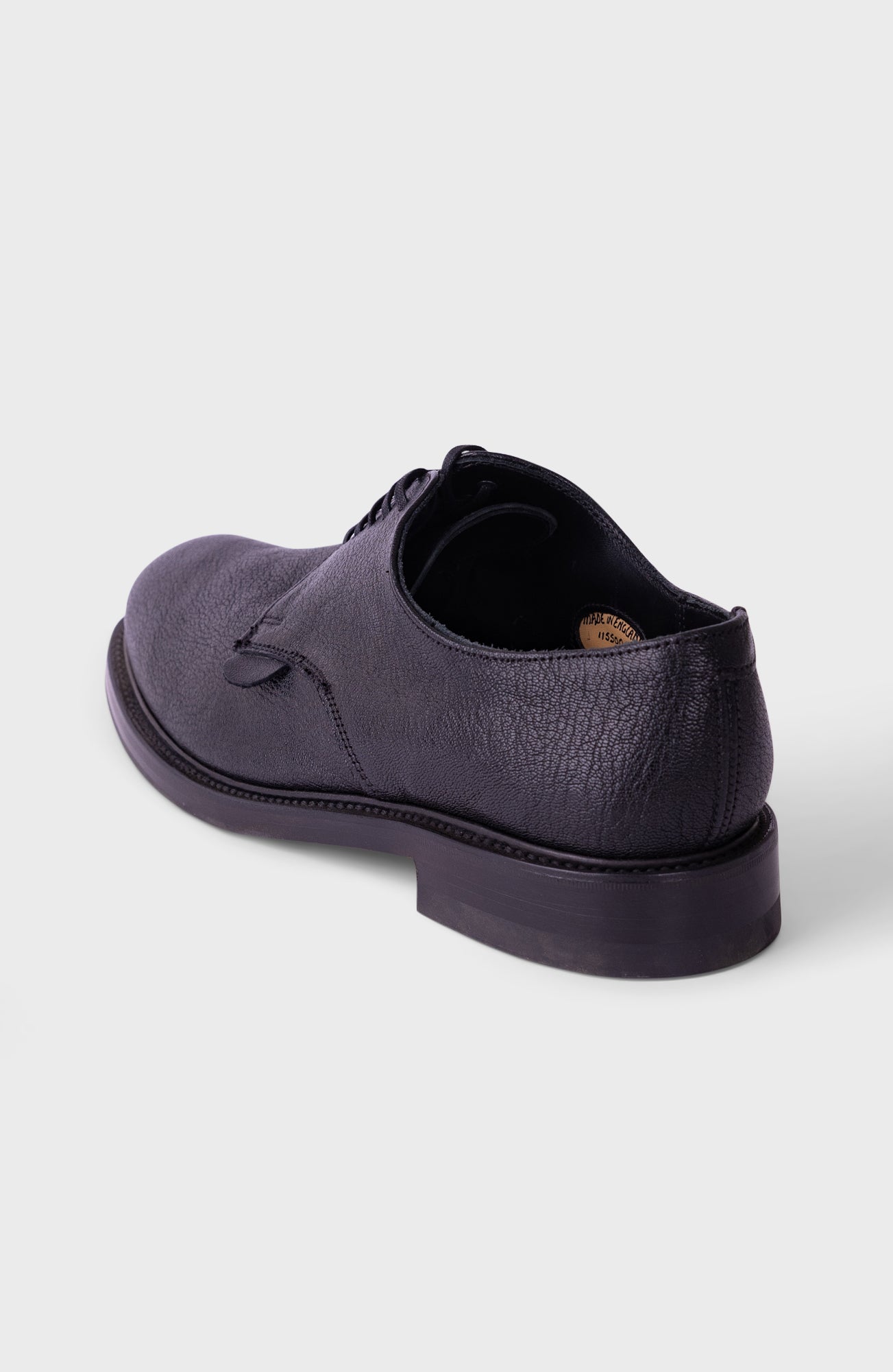 A dark purple textured leather lace-up shoe shown from a rear three-quarter angle on a light gray background.