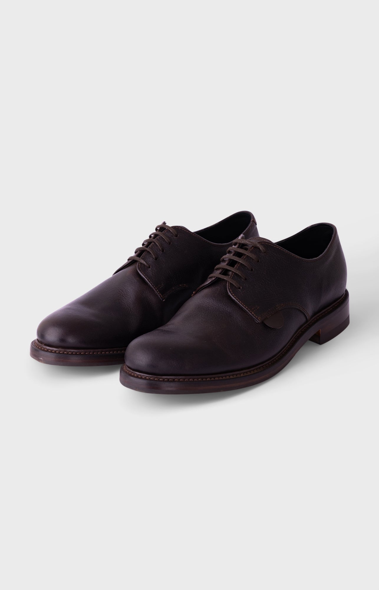 A pair of dark brown leather lace-up dress shoes with a low stacked heel, shown on a light gray background.