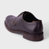 A single black leather lace-up shoe with a chunky lug sole, shown from a rear three-quarter angle on a light gray background.