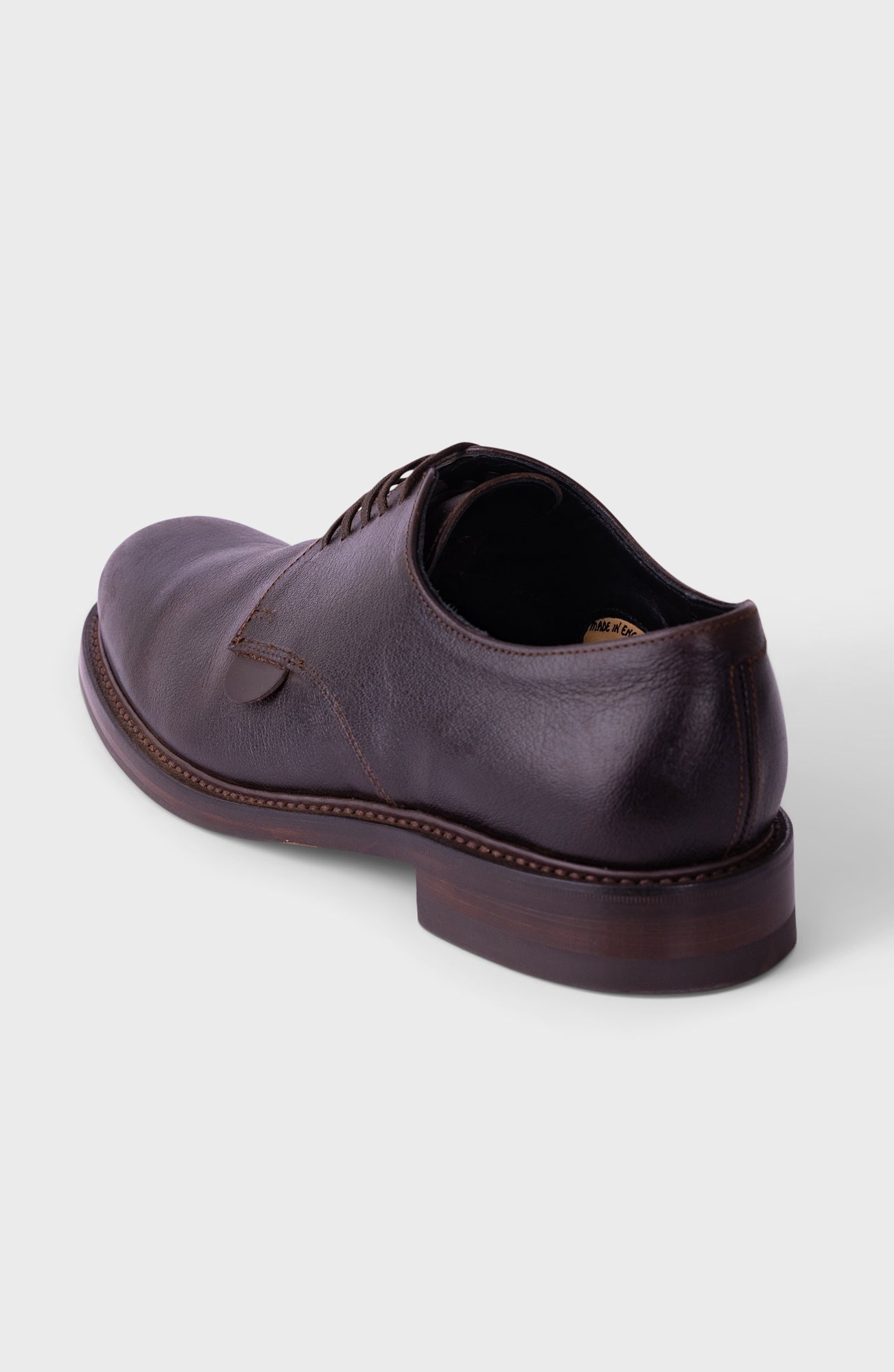 A single black leather lace-up shoe with a chunky lug sole, shown from a rear three-quarter angle on a light gray background.