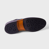 A close-up of a shoe sole showing a dark navy or black rubber outsole with circular tread patterns, a tan leather insole, and a dark purple side edge, photographed on a light gray background.