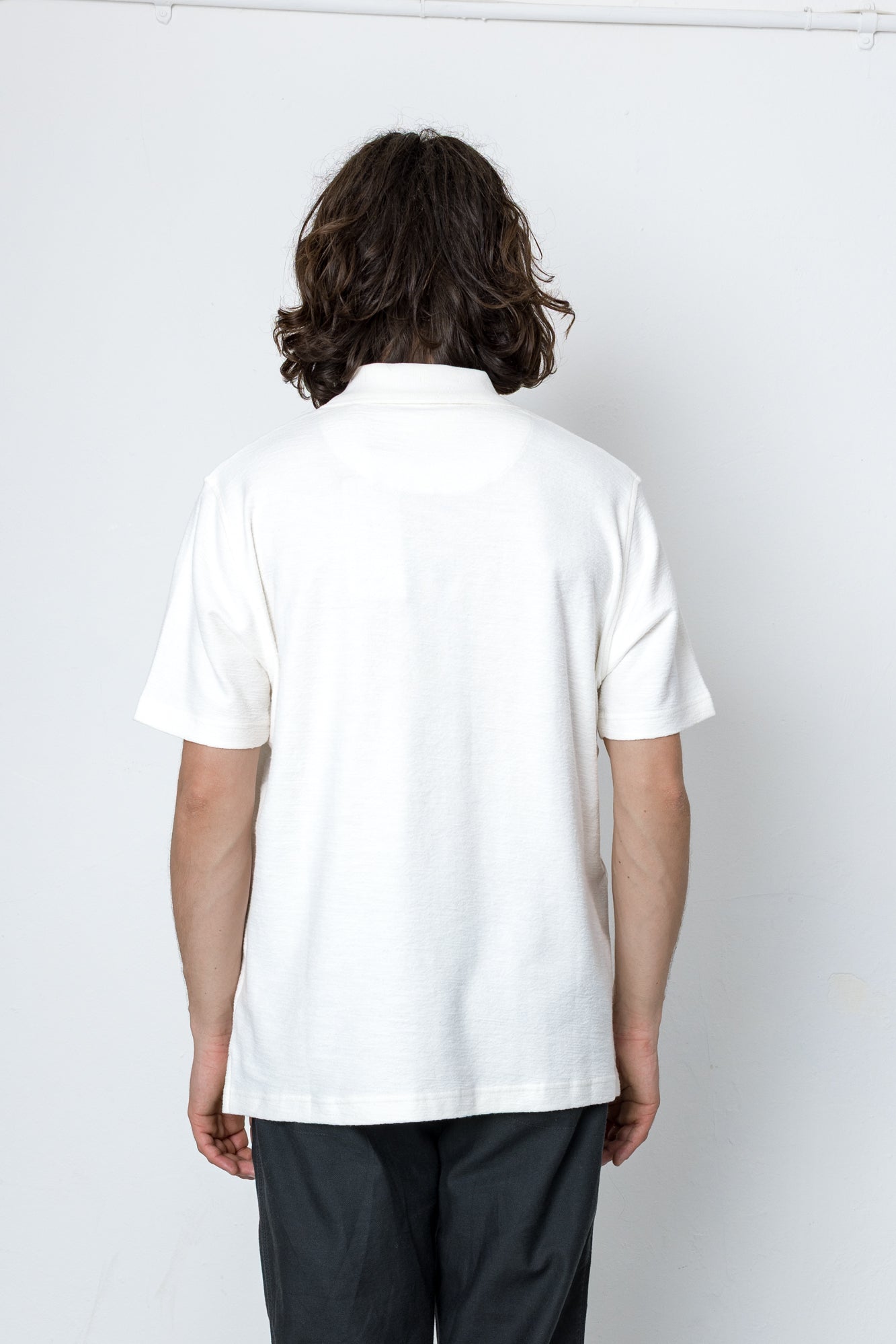 Person wearing a white polo shirt and dark pants on a white background
