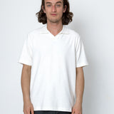 Person wearing a white polo shirt and dark pants against a plain background