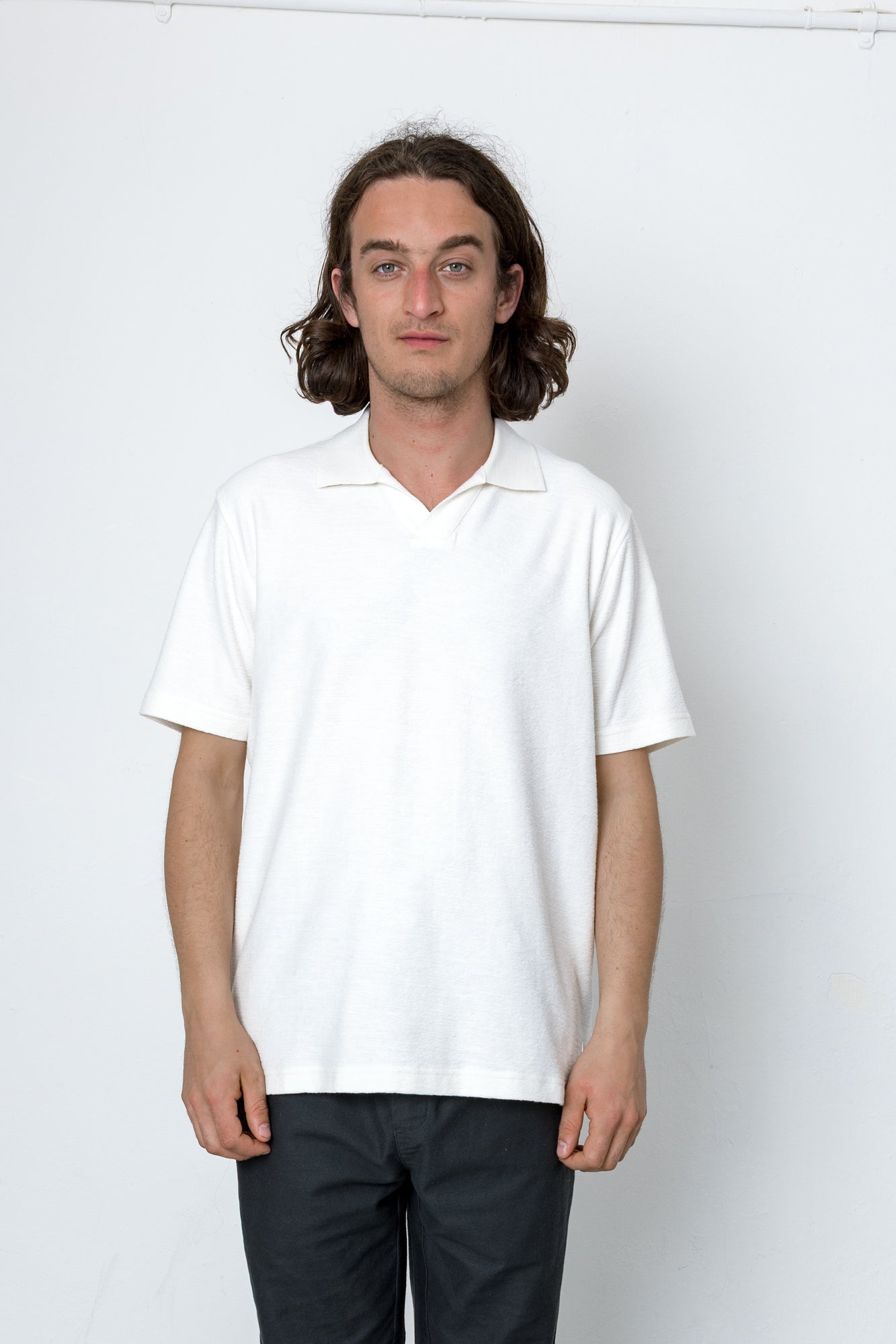 Person wearing a white polo shirt and dark pants against a plain background