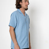 Man wearing a blue patterned shirt against a white background