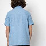 Person wearing a blue patterned shirt against a white background