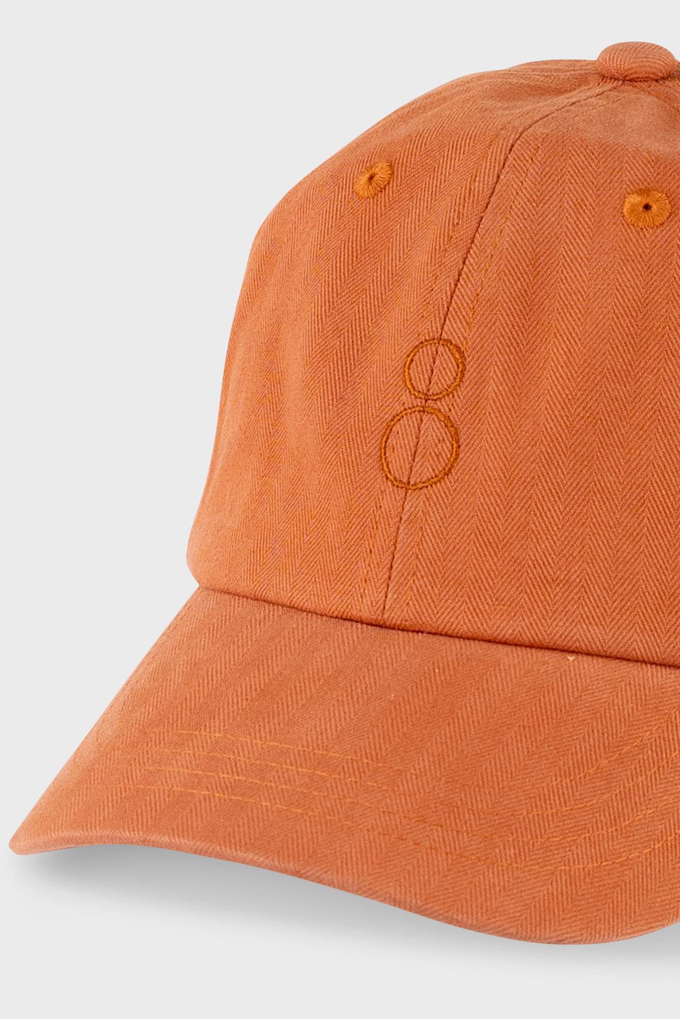 A close-up shot of a washed orange baseball cap with a tonal embroidered double-ring logo on the front, set against a light gray background.