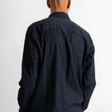 A man viewed from behind wearing a black long-sleeve button-up shirt and dark pants, standing against a plain white background.