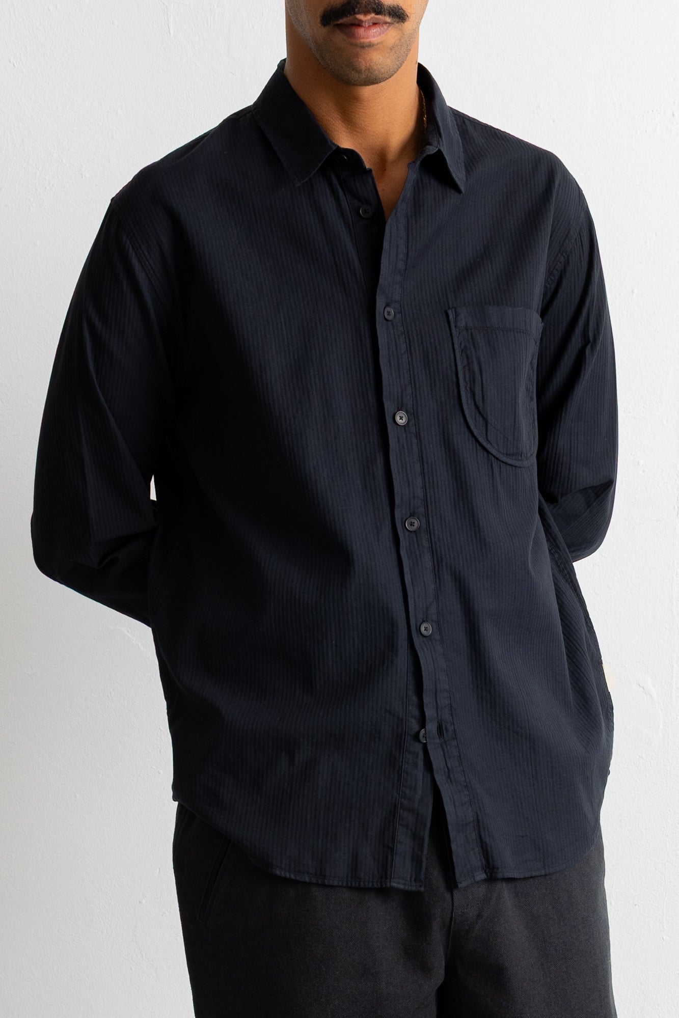 A man wearing a black long-sleeve button-down shirt with a chest pocket, shown from the chin down against a plain light background.
