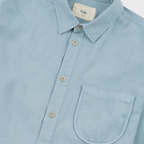 A close-up of a light blue button-down shirt with a collar, front buttons, and a chest pocket. The brand label inside the collar reads 'folk'.