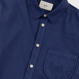 A close-up of a navy blue button-down shirt with a collar, white buttons, and a chest pocket. The brand label inside the collar reads 'Folk'.