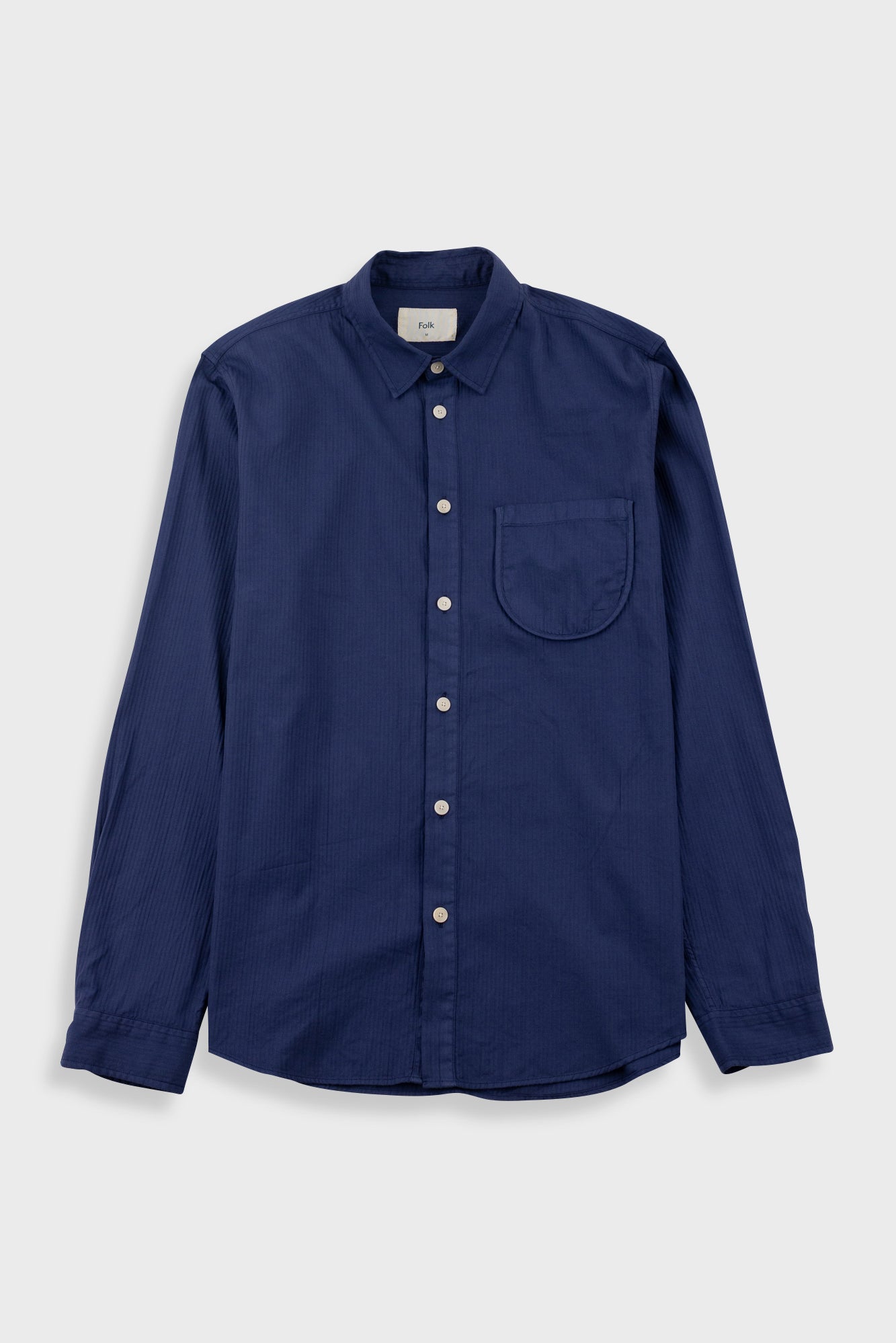 A navy blue long-sleeve button-up shirt with a single chest pocket, laid flat against a light gray background.