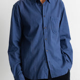 A man wearing a blue long-sleeve button-down shirt with a chest pocket, paired with dark pants, photographed against a plain light background.