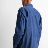 A man wearing a blue long-sleeve button-up shirt, shown from the back against a plain white studio background.