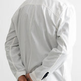 A man wearing a white long-sleeve button-up shirt, shown from the back with his hands clasped behind his back, paired with dark blue jeans against a plain white background.