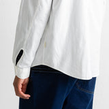 Close-up of a person wearing a white textured long-sleeve button-up shirt and dark blue jeans, showing the back of the shirt and sleeve detail against a plain light background.