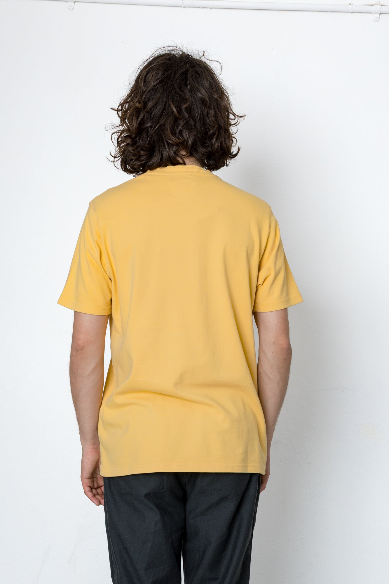 Person wearing a yellow t-shirt and black pants against a white background