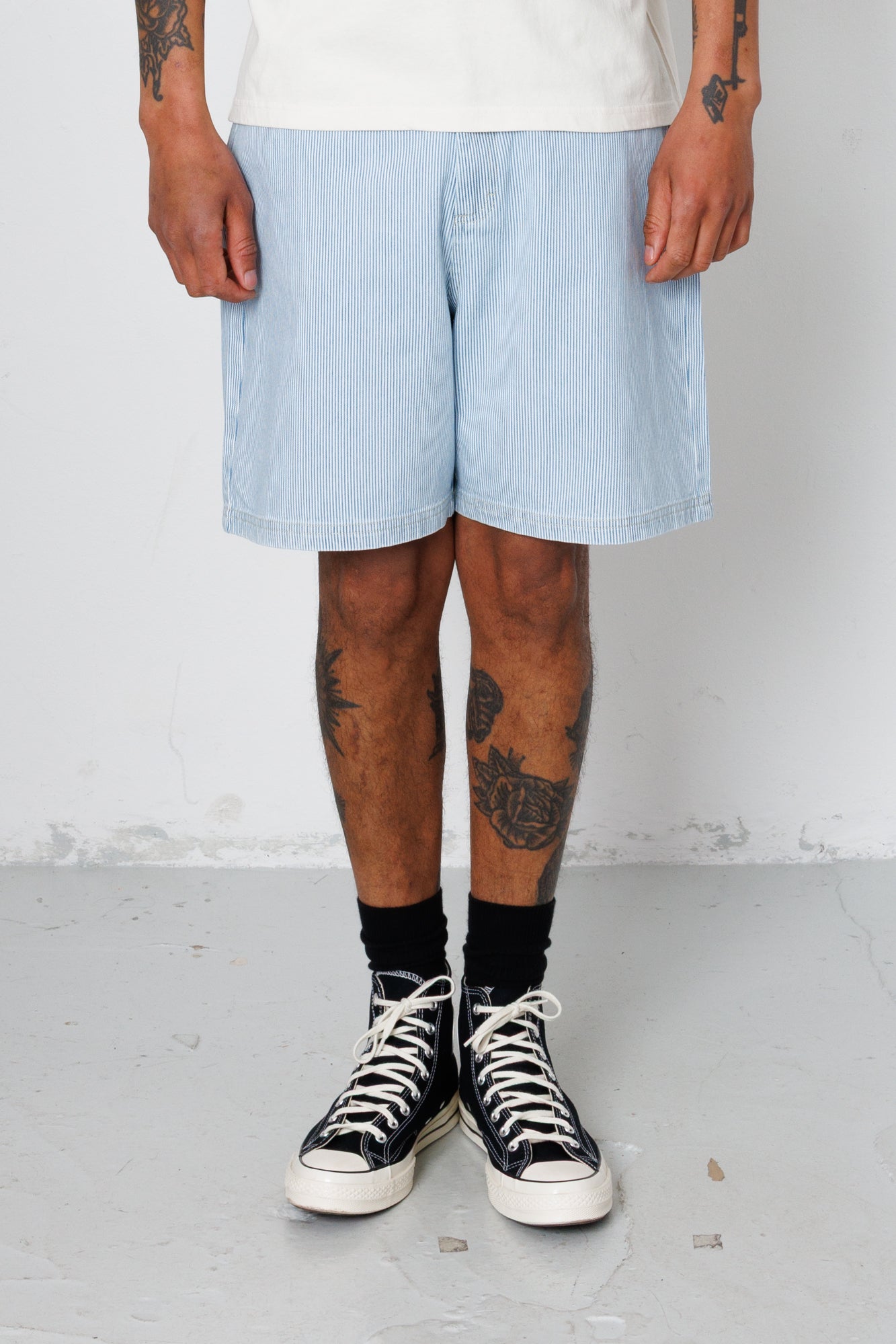 Person wearing light blue shorts and black high-top sneakers on a plain background