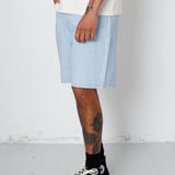 Person wearing light blue shorts, black sneakers, and a white shirt on a plain background
