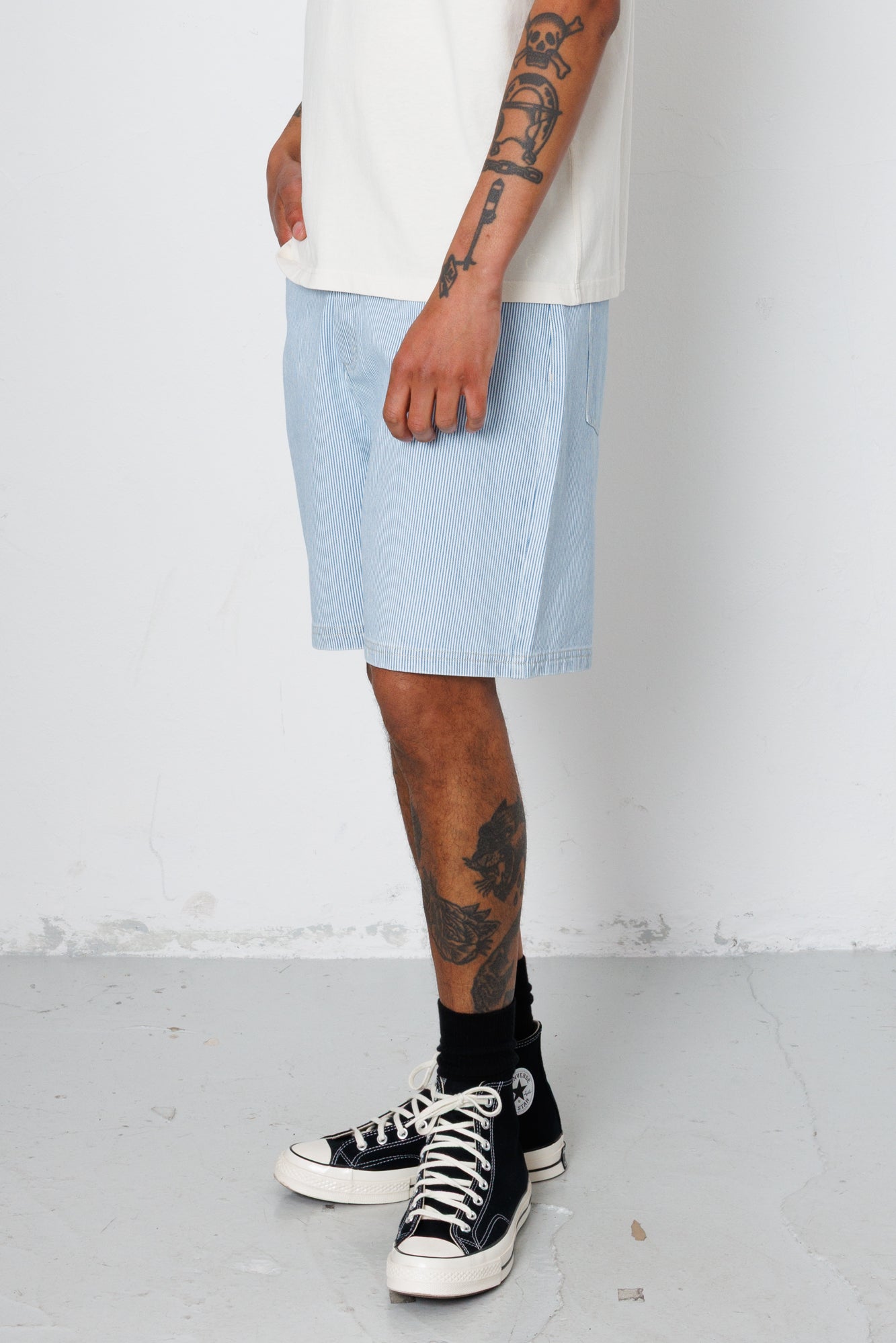 Person wearing light blue shorts, black sneakers, and a white shirt on a plain background