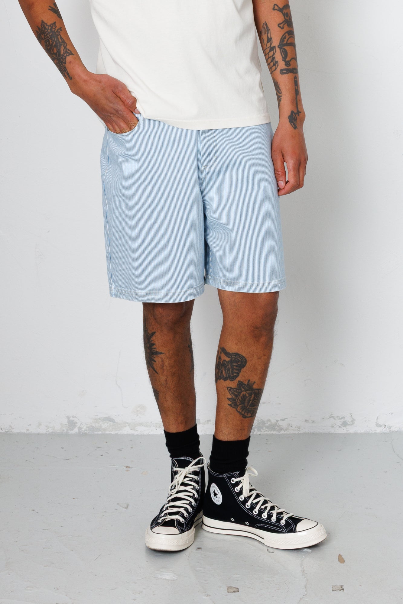Person wearing light blue shorts and black high-top sneakers on a plain background