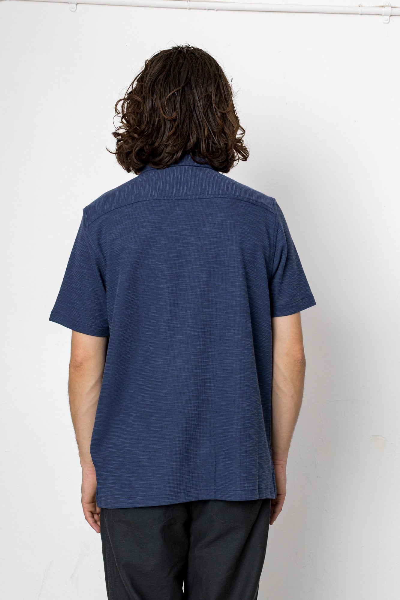Person wearing a blue shirt and black pants against a white background