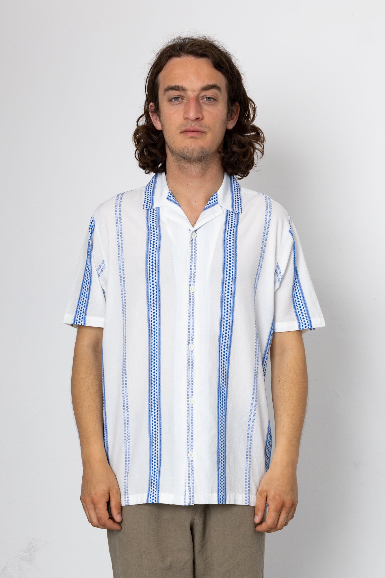Man wearing a white shirt with blue patterns on a plain background