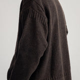 A man wearing a dark brown knit sweater, shown from a side-back angle against a plain light gray background.