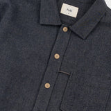 Close-up of a dark charcoal gray heathered button-down shirt with a collar, brown buttons, and a white neck label reading 'Folk'.