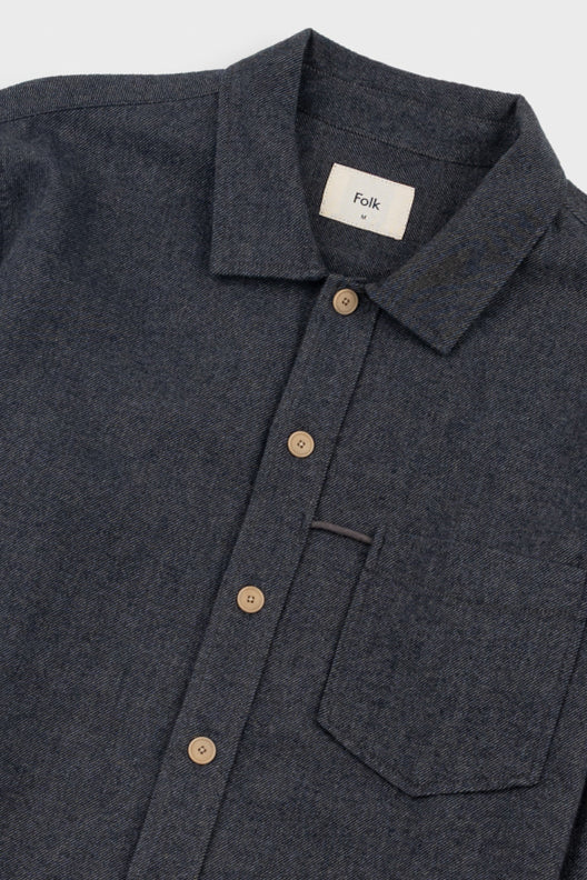 Close-up of a dark charcoal gray heathered button-down shirt with a collar, brown buttons, and a white neck label reading 'Folk'.