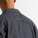 Close-up back view of a person wearing a dark charcoal gray textured overshirt or shirt jacket against a plain white wall.