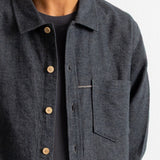 A close-up of a person wearing a dark charcoal gray textured overshirt with light brown buttons over a black t-shirt, against a plain white background.