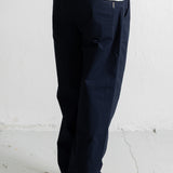 A person shown from the waist down wearing dark navy blue relaxed-fit trousers, a light blue sweatshirt, and navy canvas sneakers with white soles, standing against a white wall.