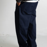 A person shown from the waist down wearing dark navy wide-leg trousers, a dark brown textured sweater, and black canvas sneakers against a light gray studio wall.