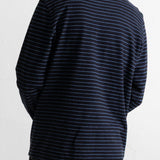 A person shown from the back wearing a navy long-sleeve shirt with thin white horizontal stripes and black corduroy pants against a plain white wall.