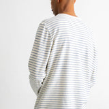 A man viewed from behind wearing a white long-sleeve t-shirt with thin dark horizontal stripes and dark blue jeans, set against a plain white background.