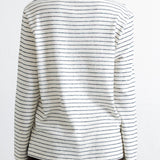 A person shown from the back wearing a long-sleeve knit top with thin dark horizontal stripes on an off-white base, paired with dark brown corduroy pants, against a plain white background.
