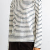 A woman wearing a long-sleeve crewneck shirt with thin dark horizontal stripes on an off-white base, paired with dark brown corduroy pants, against a plain white background.