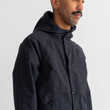 A man wearing a black hooded jacket, shown in a side profile against a plain white wall.