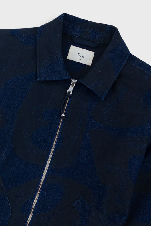Close-up of a dark blue jacket with a zipper and 'Folk' label on a light gray background
