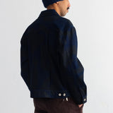 A man wearing a dark navy blue jacket, a matching navy blue knit beanie, and brown corduroy trousers, photographed from the back against a plain white wall.