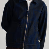 A man wearing a dark navy blue zip-up jacket with a subtle tonal pattern, layered over a white t-shirt and brown corduroy trousers, photographed against a neutral light gray background.