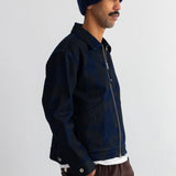 A man wearing a dark navy blue zip-up jacket, a matching navy knit beanie, and brown corduroy pants, shown in profile against a plain white wall.